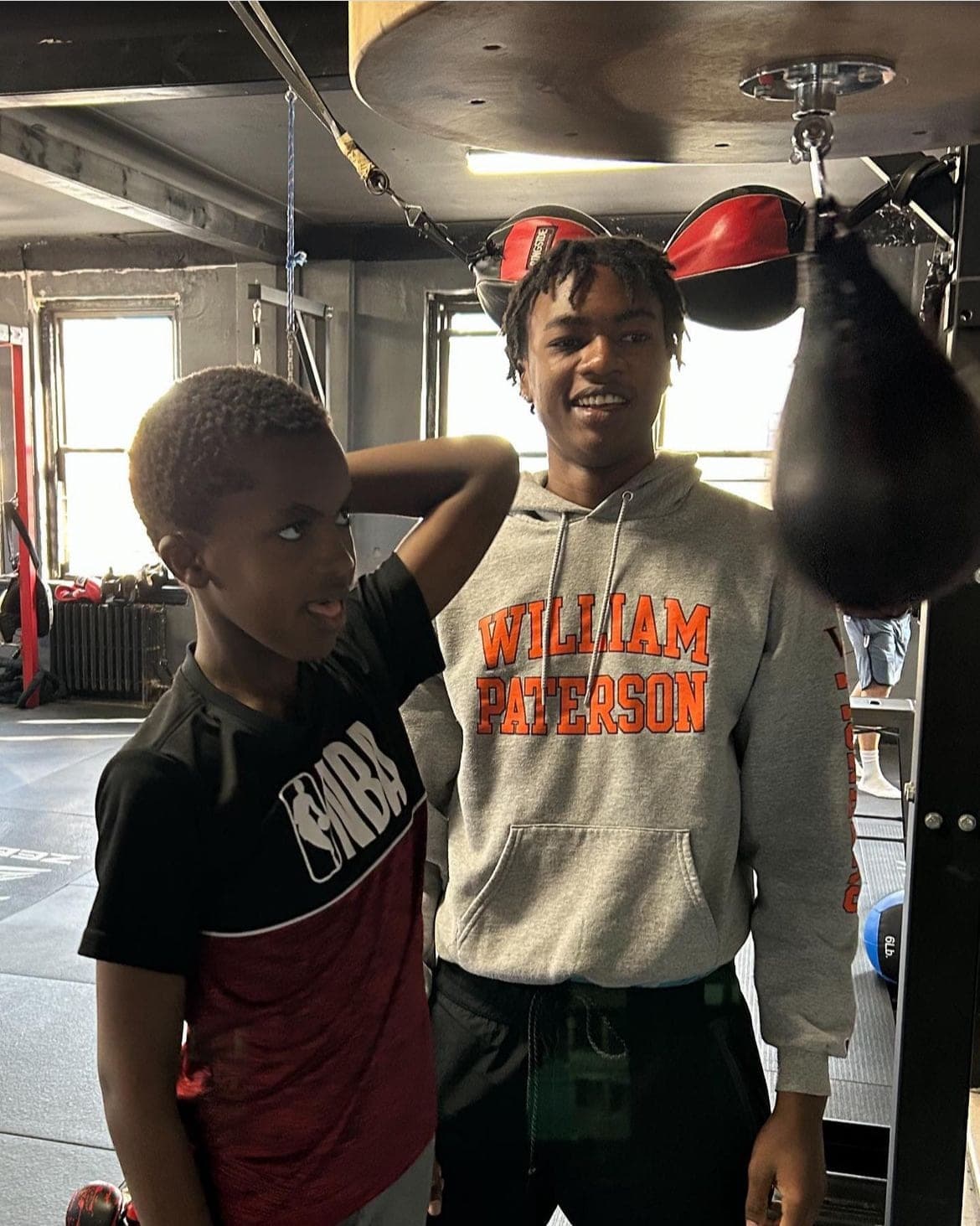 A young student and a coach standing together under the speed bag in the gym